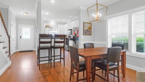 Un comedor amplio con una mesa y sillas de madera, un candelabro y vista a la cocina al fondo.