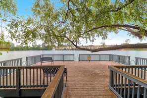 Eine Holzterrasse mit Metallgeländern, einer Bank und einem Tisch mit Blick auf ruhiges Wasser.