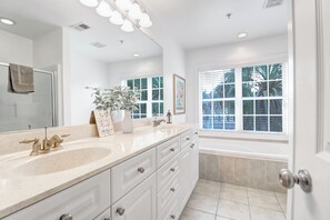 A modern bathroom with a large vanity, a bathtub, and a window with blinds.