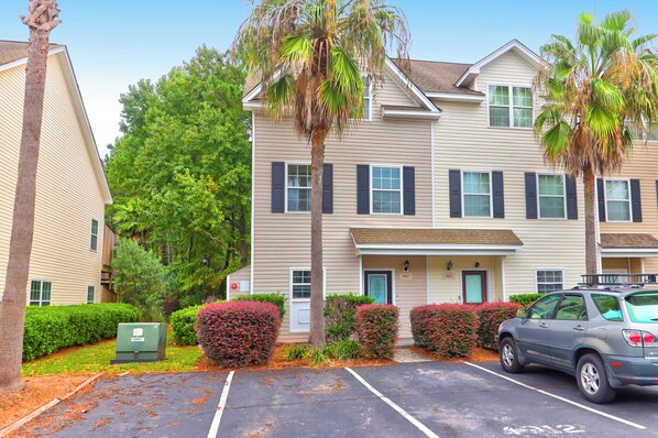 A multi-story residential building with a parking lot, palm trees, and a car parked in the lot.