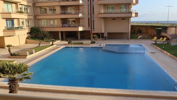 A swimming pool with a view of a multi-story building, a small garden area, and a distant view of the sea. - Pool and sea view accommodation 50 m sea (Ovar)