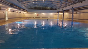 An indoor swimming pool with a clear ceiling and walls, equipped with safety equipment and lighting. - Pool and sea view accommodation 50 m sea (Ovar)