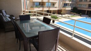 A balcony with a glass-top table and wicker chairs, overlooking a swimming pool and adjacent buildings. - Pool and sea view accommodation 50 m sea (Ovar)