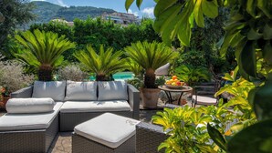A patio area with wicker furniture, a round table with fruit, and lush greenery. - Garden Tower Relais Sorrento (Sorrento)