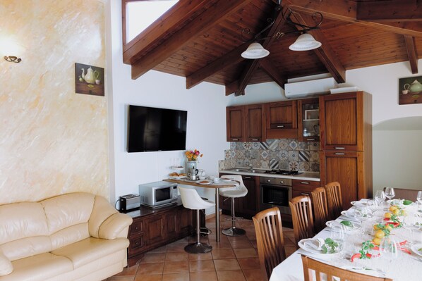 A compact kitchen with wooden cabinets, a dining area with a table set for four, and a sofa in the living area.