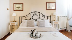 A neatly made bed with a tray of tea and sugar, two bedside tables with lamps, and two framed pictures on the wall. - Garden Tower Relais Sorrento (Sorrento)