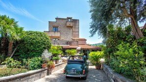 A vintage car parked in front of a stone building with balconies, surrounded by lush greenery and potted plants. - Garden Tower Relais Sorrento (Sorrento)