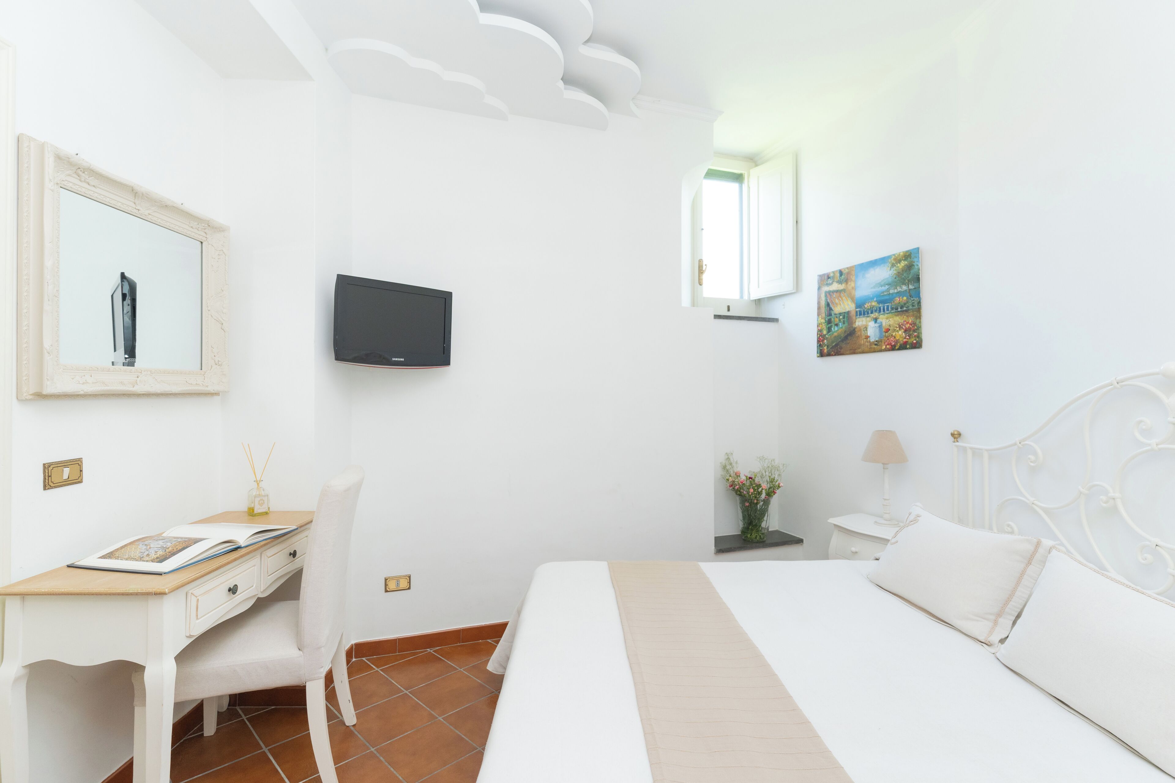 Une chambre à coucher avec un lit, un bureau, une chaise, une télévision, un tableau et une fenêtre.