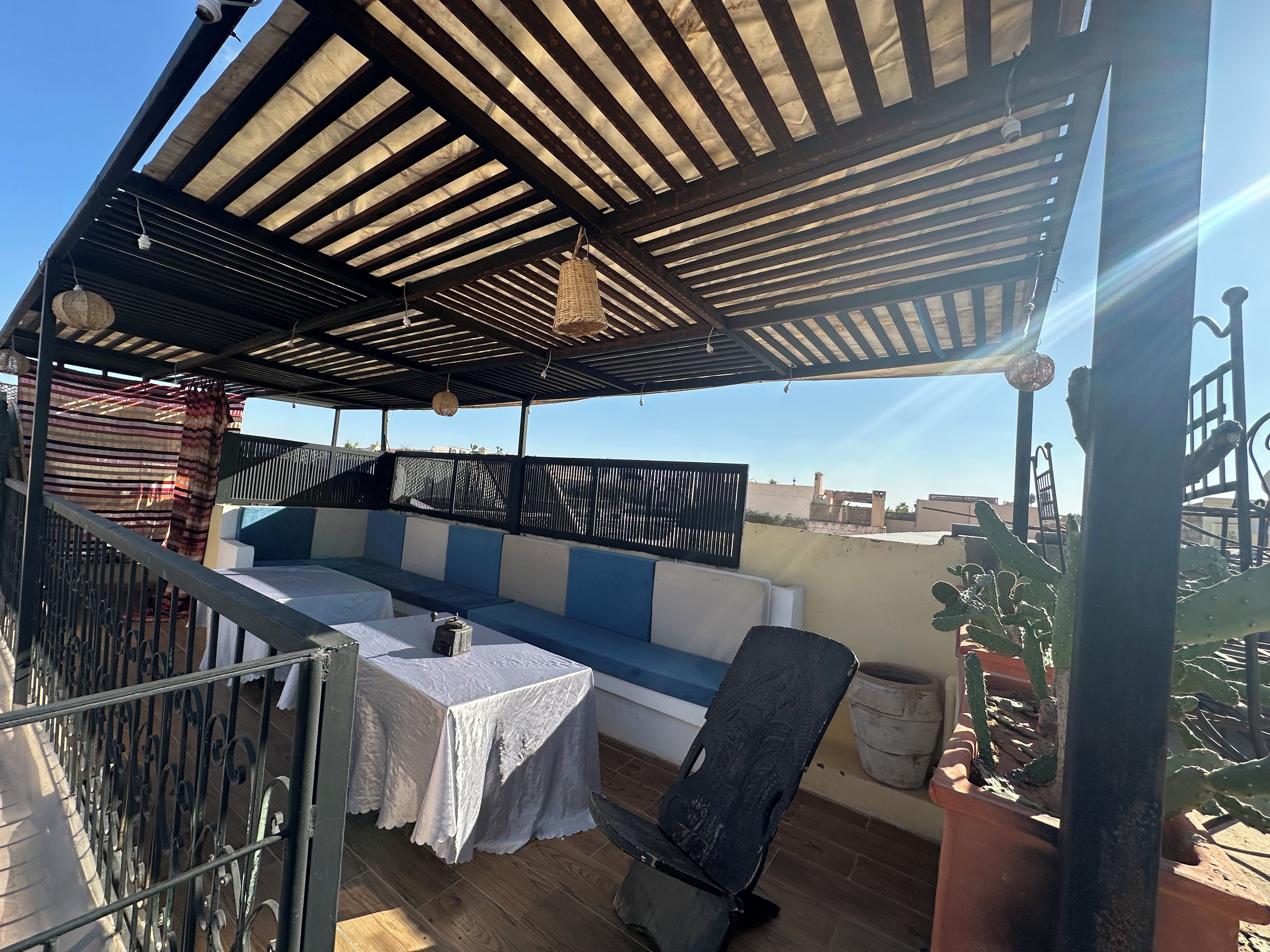 Un espace extérieur abrité, aménagé avec une table et des chaises, une rambarde en métal et offrant une vue sur le paysage urbain.