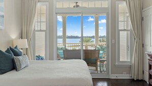 Ein Schlafzimmer mit einem großen Bett, Blick auf einen See und einem Balkon mit Gartenmöbeln.