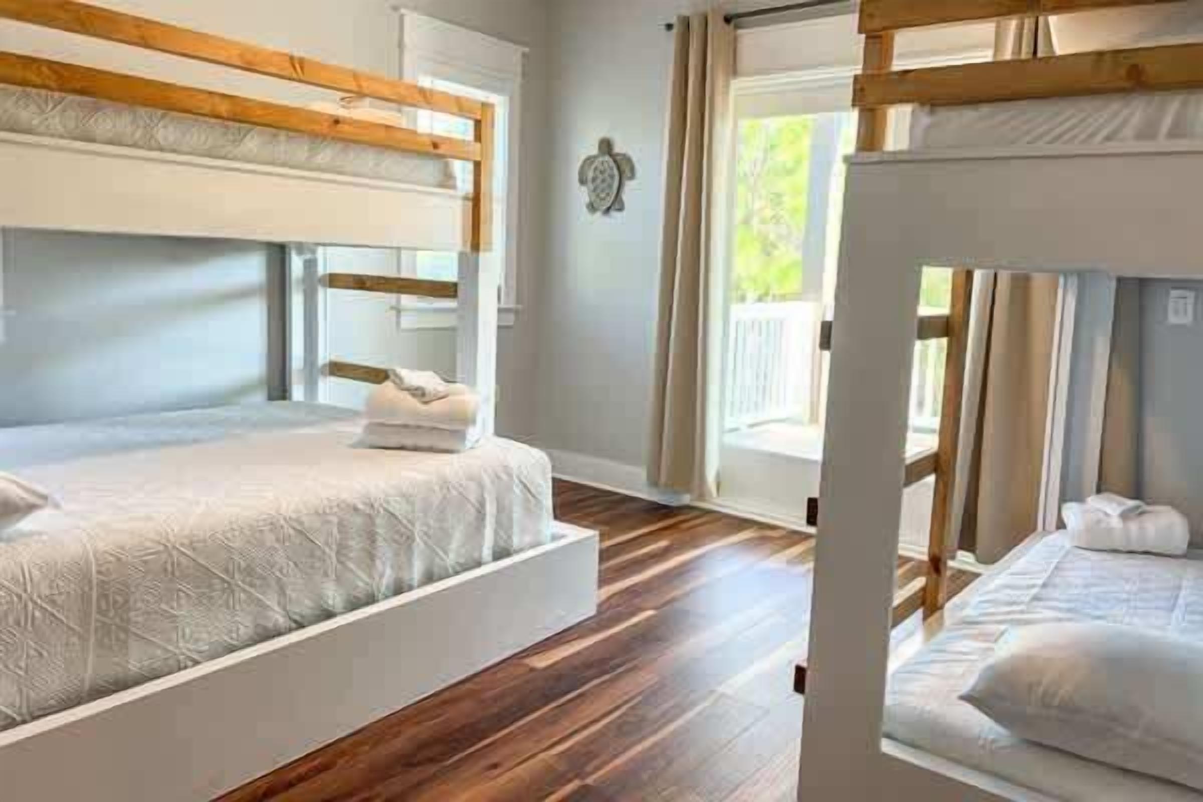 A room with two bunk beds, wooden beams on the ceiling, a window with curtains, and a small wall decoration.