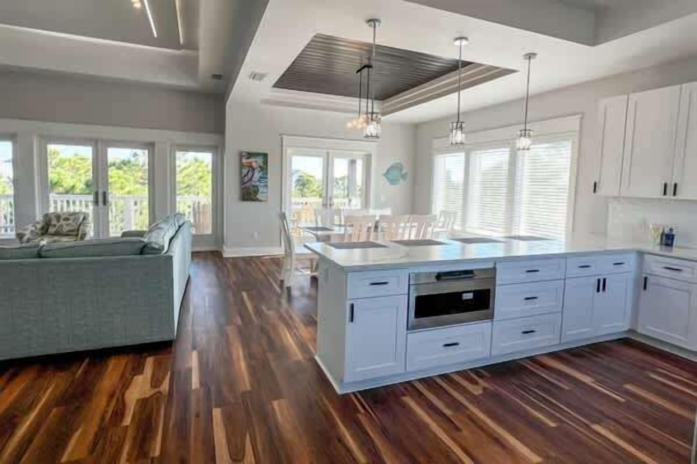 A spacious kitchen with a large island, white cabinetry, and a dining area with a gray sofa.