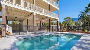 A rectangular swimming pool with a clear blue water surface, surrounded by a tiled deck and a metal fence. - Pelican Point- New construction- Sleeps 11- Pool (St George Island)