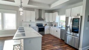 A modern kitchen with white cabinets, stainless steel appliances, and a wooden floor. - Pelican Point- New construction- Sleeps 11- Pool (St George Island)