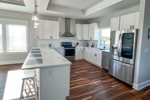 A modern kitchen with white cabinets, stainless steel appliances, and a wooden floor.