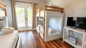 Une chambre avec des lits superposés, un téléviseur posé sur un meuble et une porte-fenêtre coulissante donnant sur un espace extérieur.