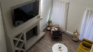 A modern living room with a fireplace, a flat-screen TV, a round coffee table, and a yellow sofa.