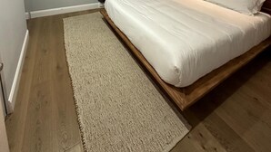 A modern bedroom with a wooden bed frame, a white mattress, a beige rug, and a wall-mounted air conditioner.
