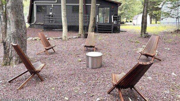 A rustic cabin with a deck area featuring four wooden chairs and a metal fire pit.