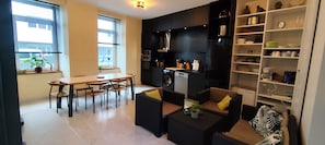 A modern kitchen with a dining area, a sofa, and a bookshelf.