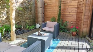 Une terrasse avec un mur en pierre, une clôture en bois et un espace détente agrémenté de coussins.