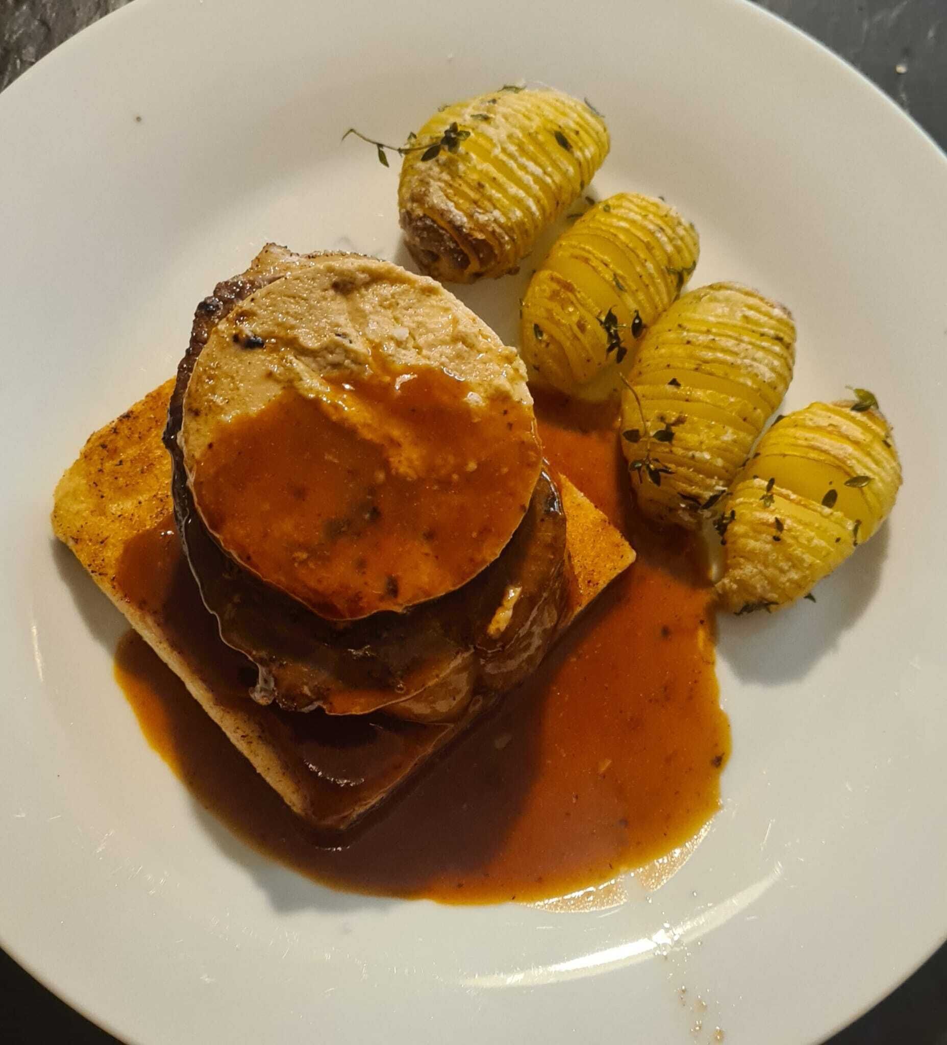 A plate with a steak topped with a creamy sauce, accompanied by roasted potatoes.