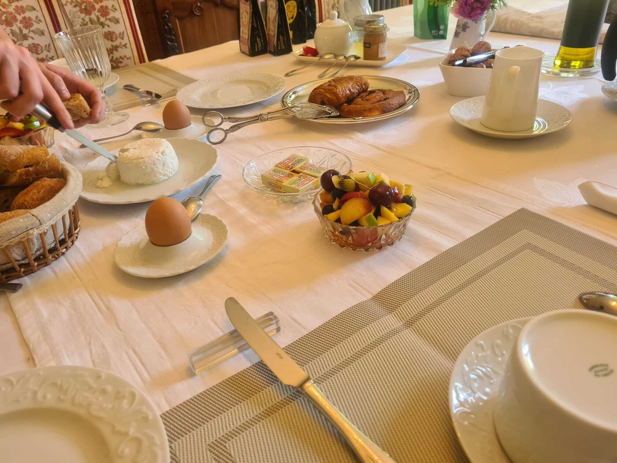 A breakfast table with plates of food, a basket of bread, and a bowl of fruit.