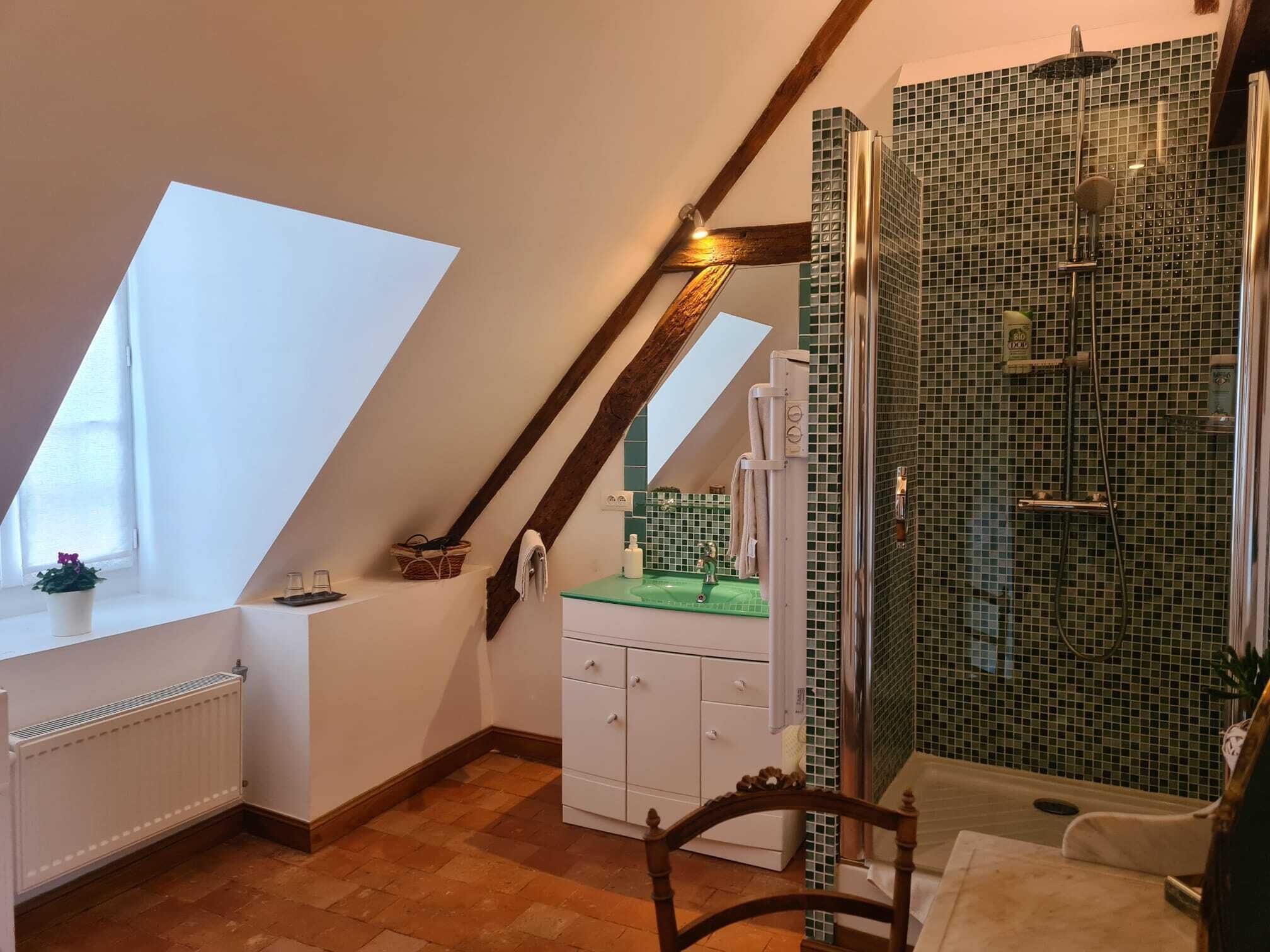 A small, sloped room with a skylight, a shower with mosaic tiles, and a wooden chair.