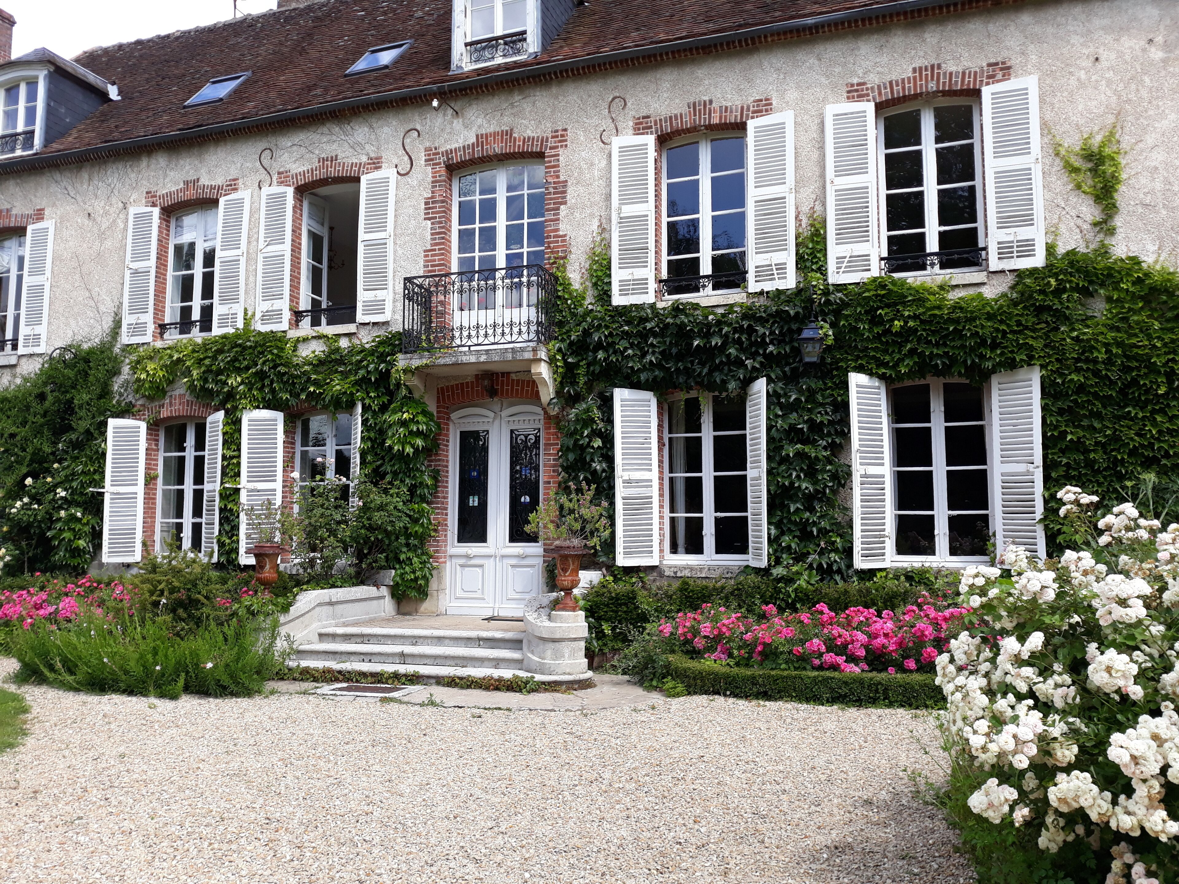 A two-story house with white shutters, a balcony, and a gravel driveway.