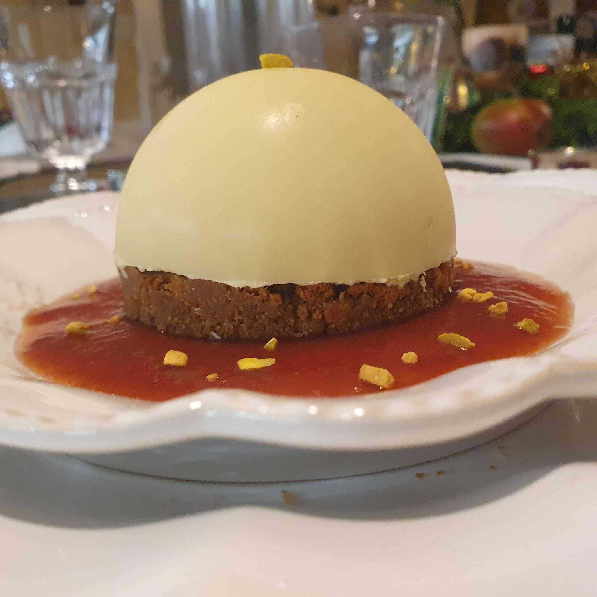 A dessert on a white plate with a red sauce and lemon zest garnish.