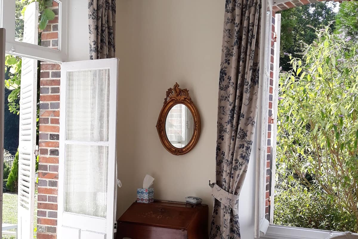 Una habitación con candelabro, un escritorio de madera, una silla, un radiador y una ventana con cortinas.
