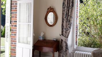A room with a chandelier, a wooden desk, a chair, a radiator, and a window with curtains.