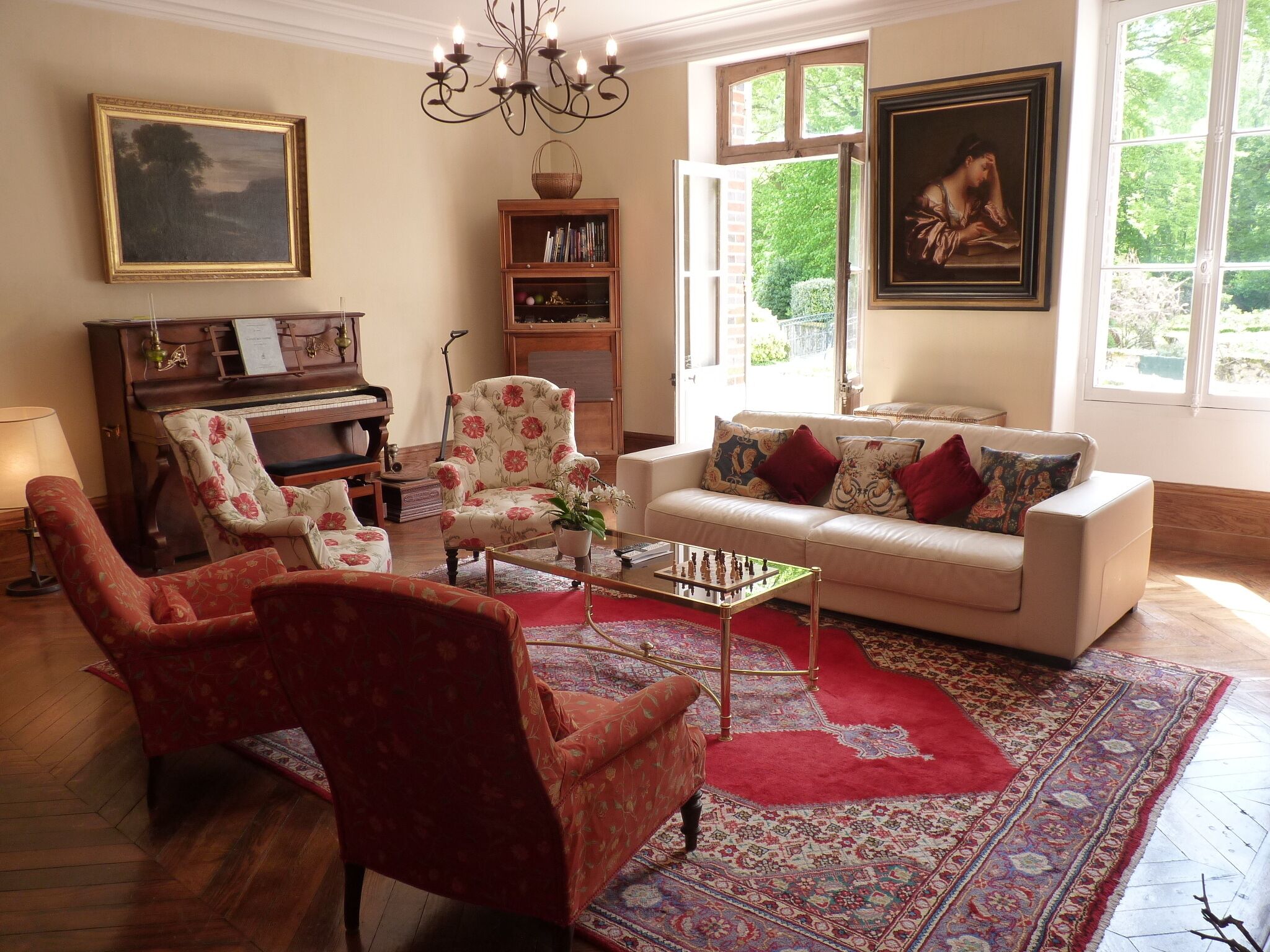A living room with a piano, a sofa, a red armchair, a coffee table, and a bookshelf.