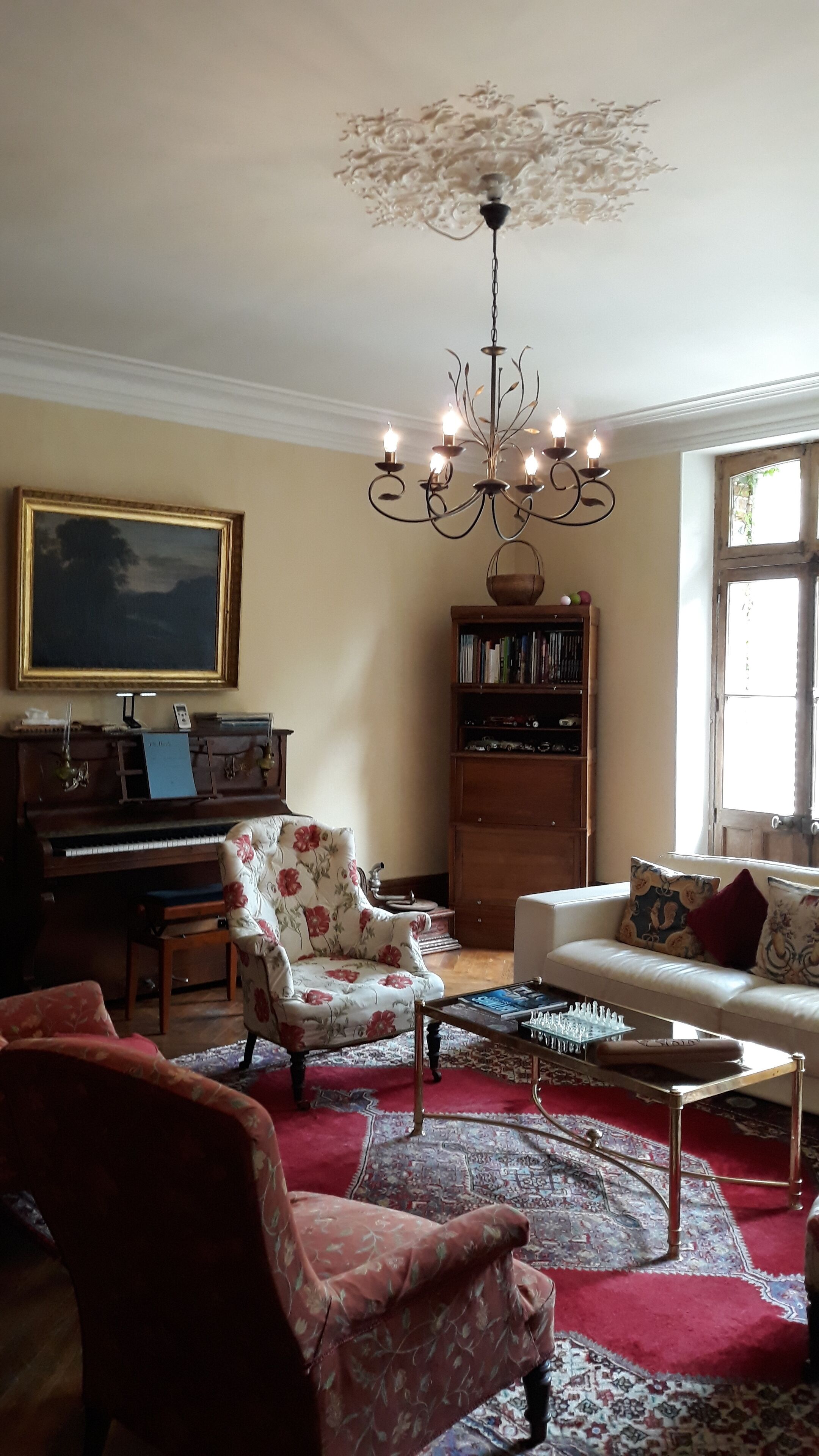 A living room with a piano, a floral armchair, a sofa, a coffee table, and a bookshelf.