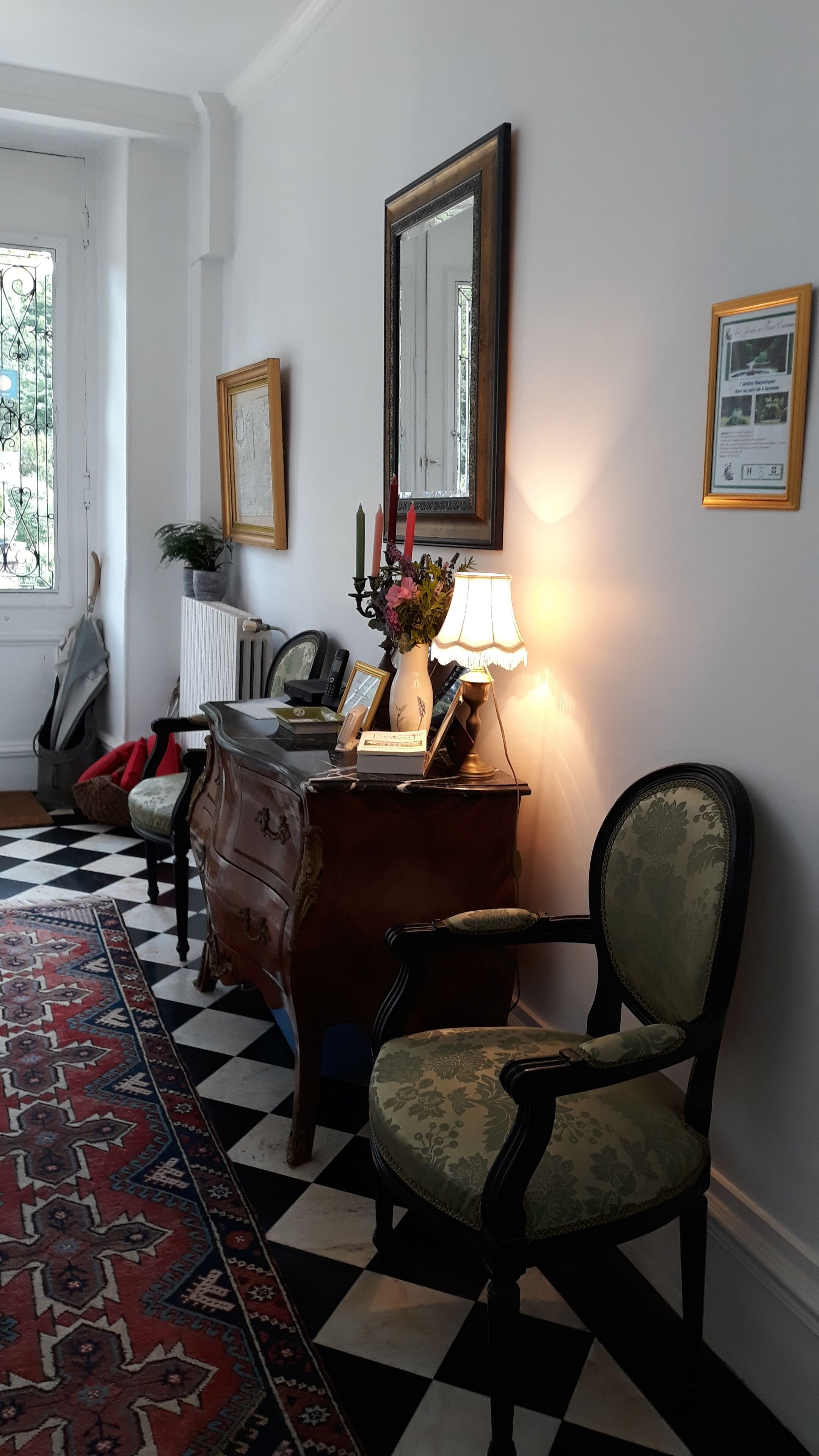 A room with a checkered floor, a wooden dresser, a chair, a lamp, a mirror, and a framed picture on the wall.