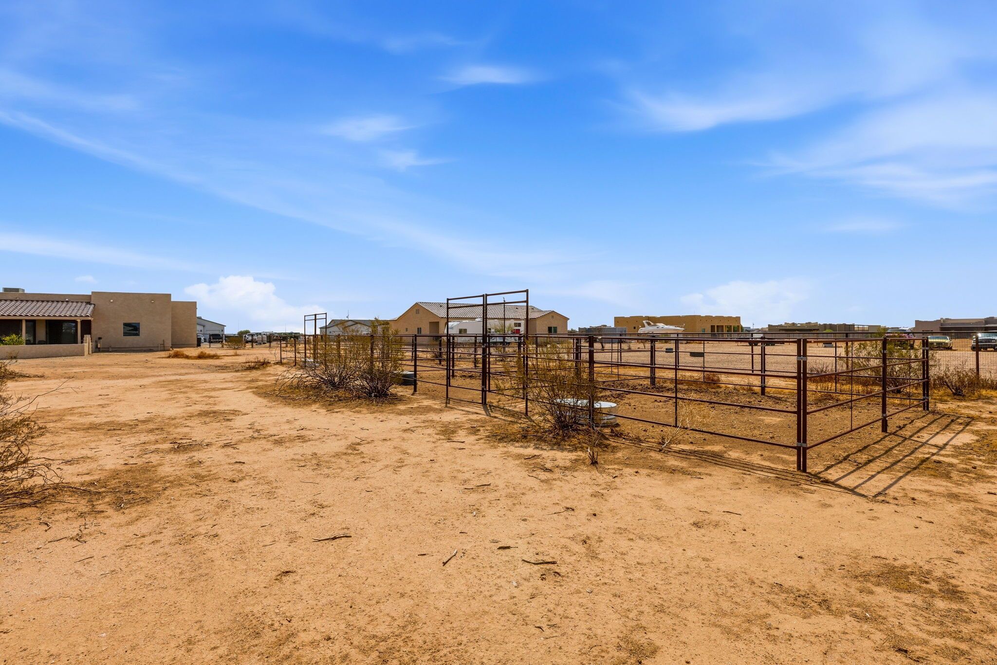 A desert landscape with sparse vegetation, a fenced area, and buildings in the background.