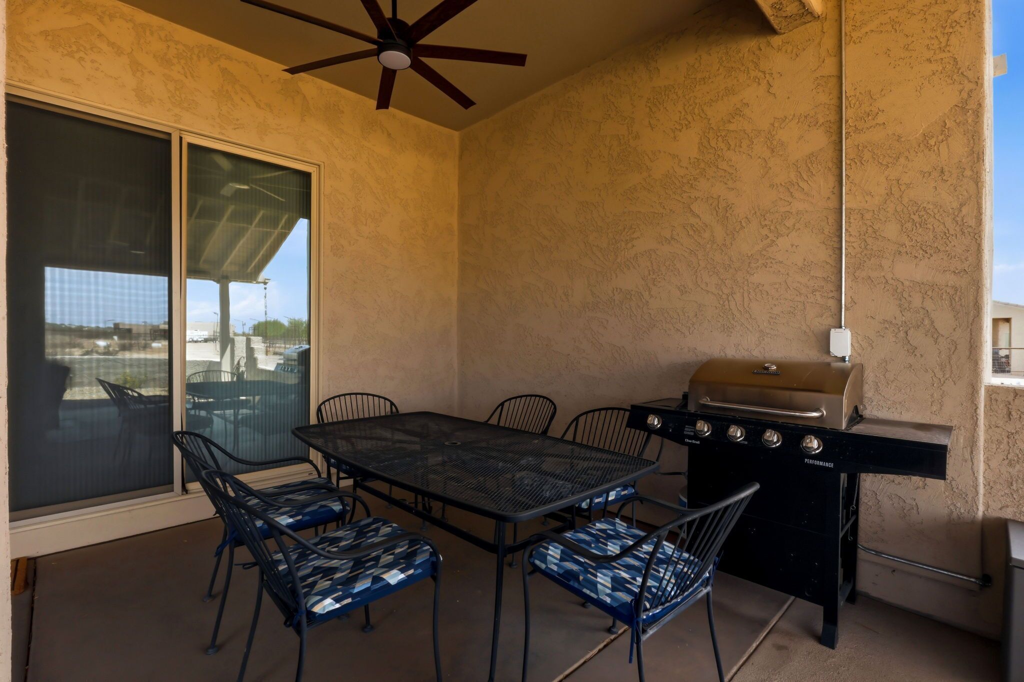 Un patio exterior con una mesa, sillas, una parrilla y un ventilador de techo.