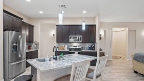 A modern kitchen with dark cabinets, stainless steel appliances, and a marble island with two chairs.