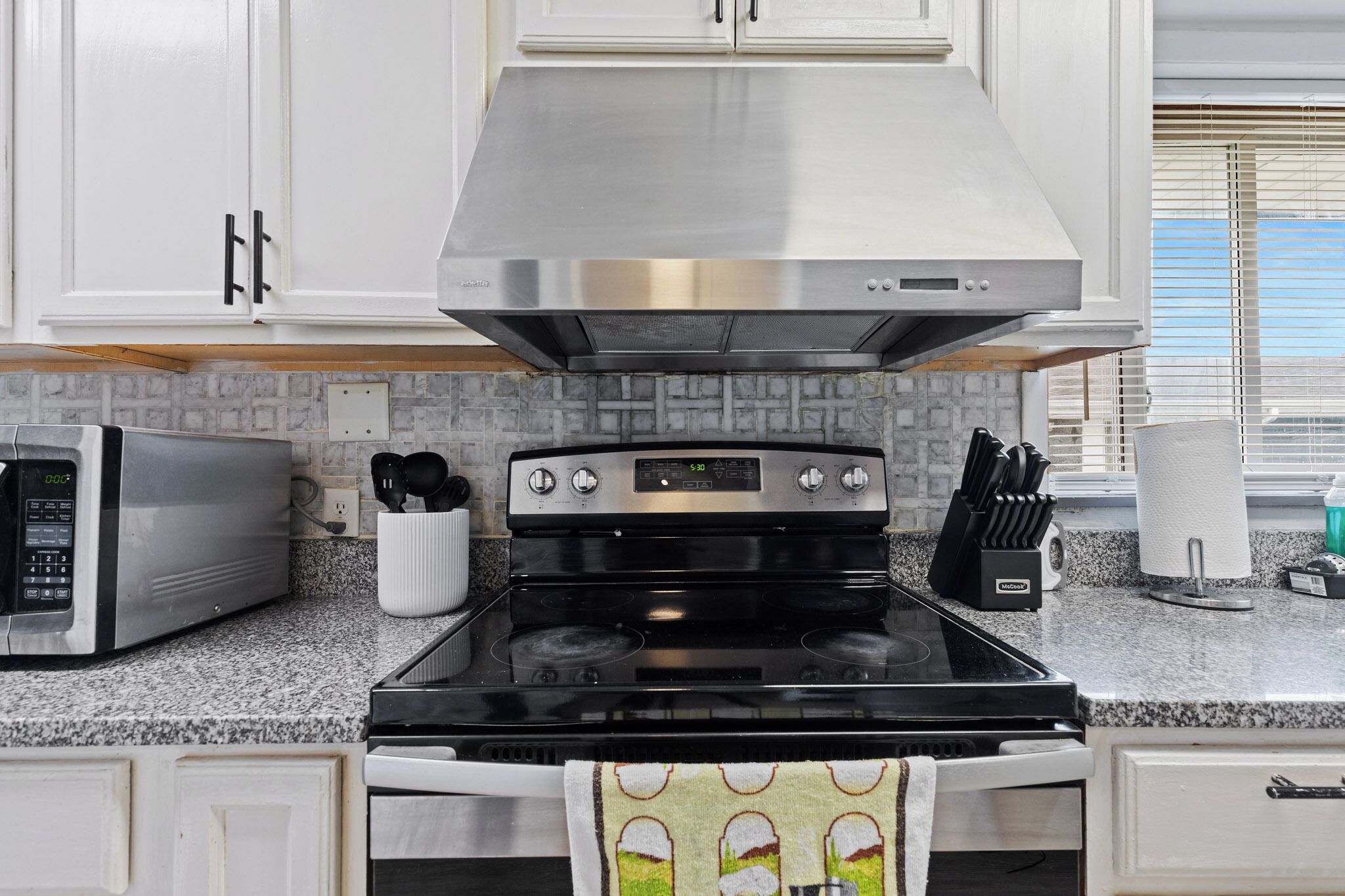 A kitchen with white cabinets, a stainless steel range hood, a microwave, and a stove.