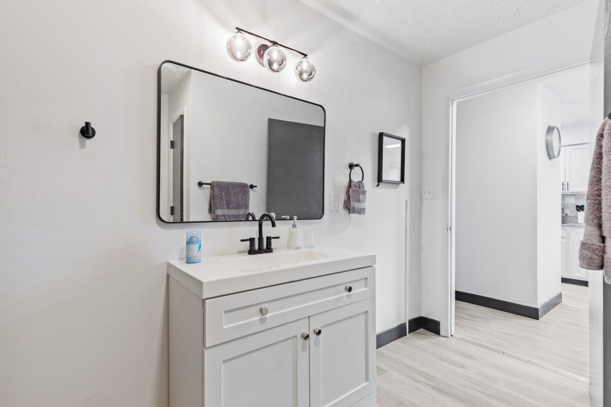 Un baño moderno con tocador blanco, un espejo grande y una lámpara sobre el espejo.