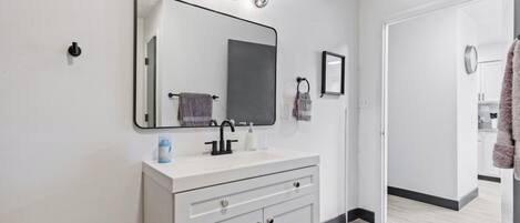 Un baño moderno con tocador blanco, un espejo grande y una lámpara sobre el espejo.