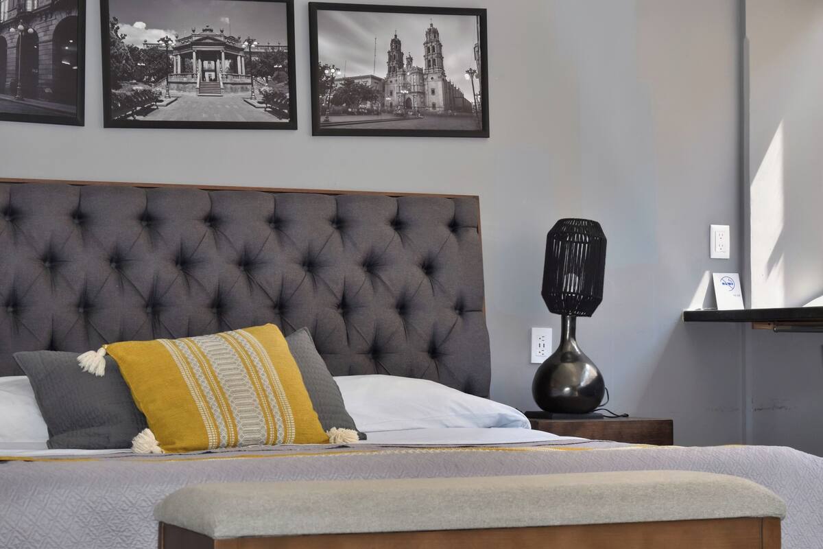 A neatly made bed with a tufted headboard, a bedside lamp, and a picture frame on the wall.