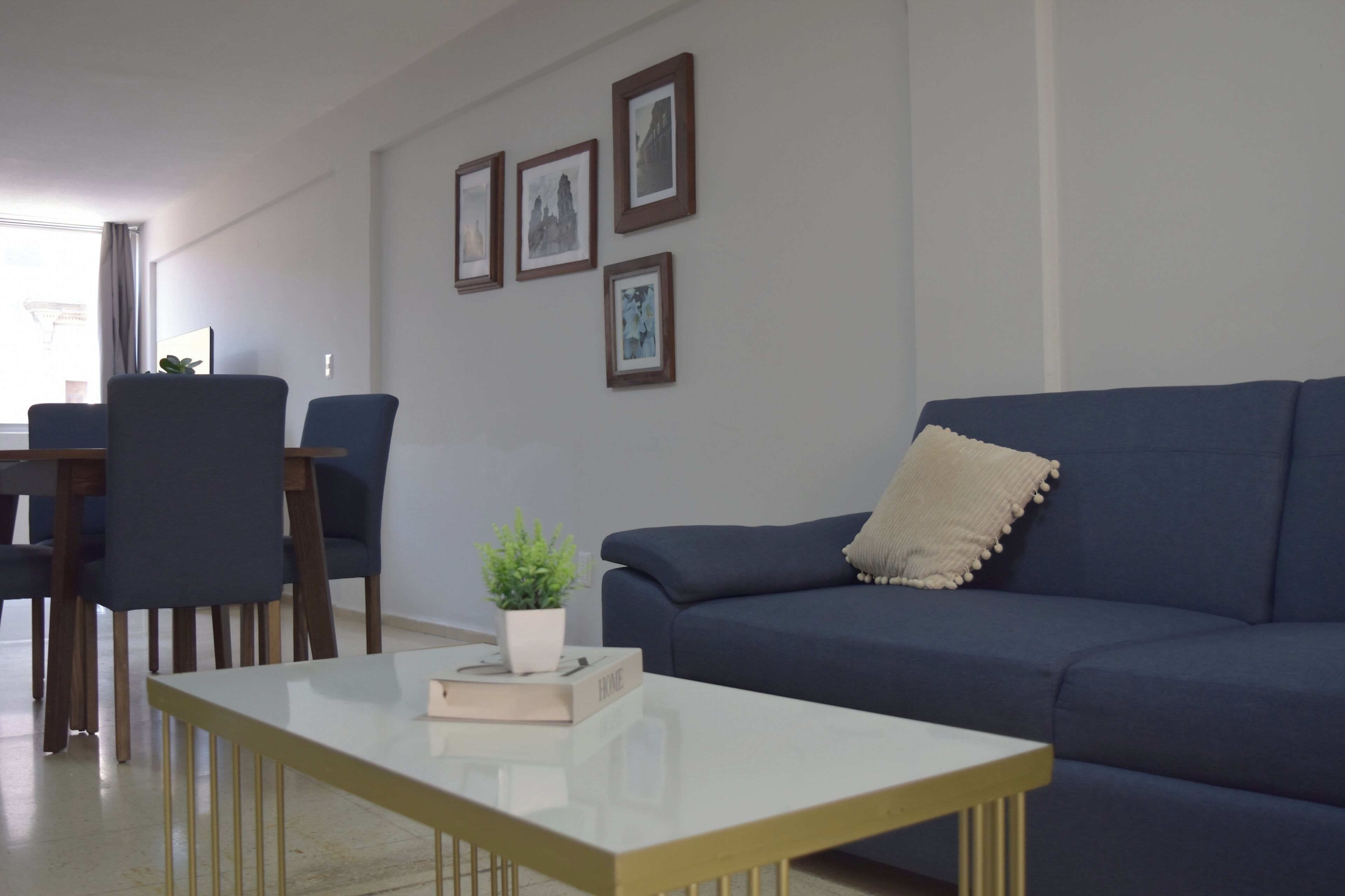 A living room with a blue sofa, a white coffee table, and a dining area with chairs and a table.