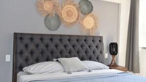 A bedroom with a tufted headboard, a bed with white bedding, a bedside table with a lamp, and wall art.