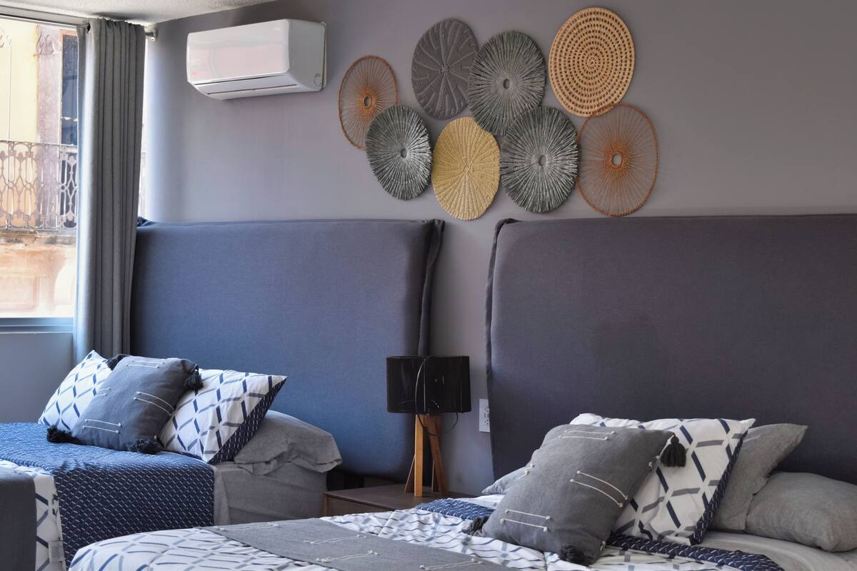 A hotel room with two beds, a wall-mounted air conditioner, and a decorative wall art piece.
