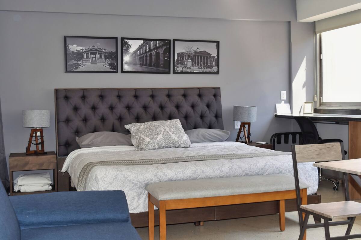A bedroom with a large bed, a desk, and a chair. There are three framed pictures on the wall.