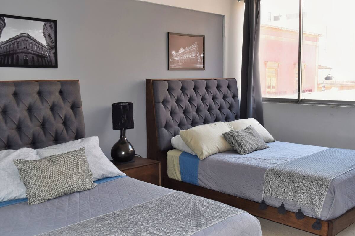 Two twin beds with grey headboards, a bedside table with a lamp, and a framed picture on the wall.