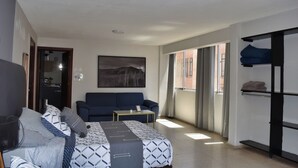 A modern hotel room with a bed, a sofa, a small table, a painting, and a window with curtains.