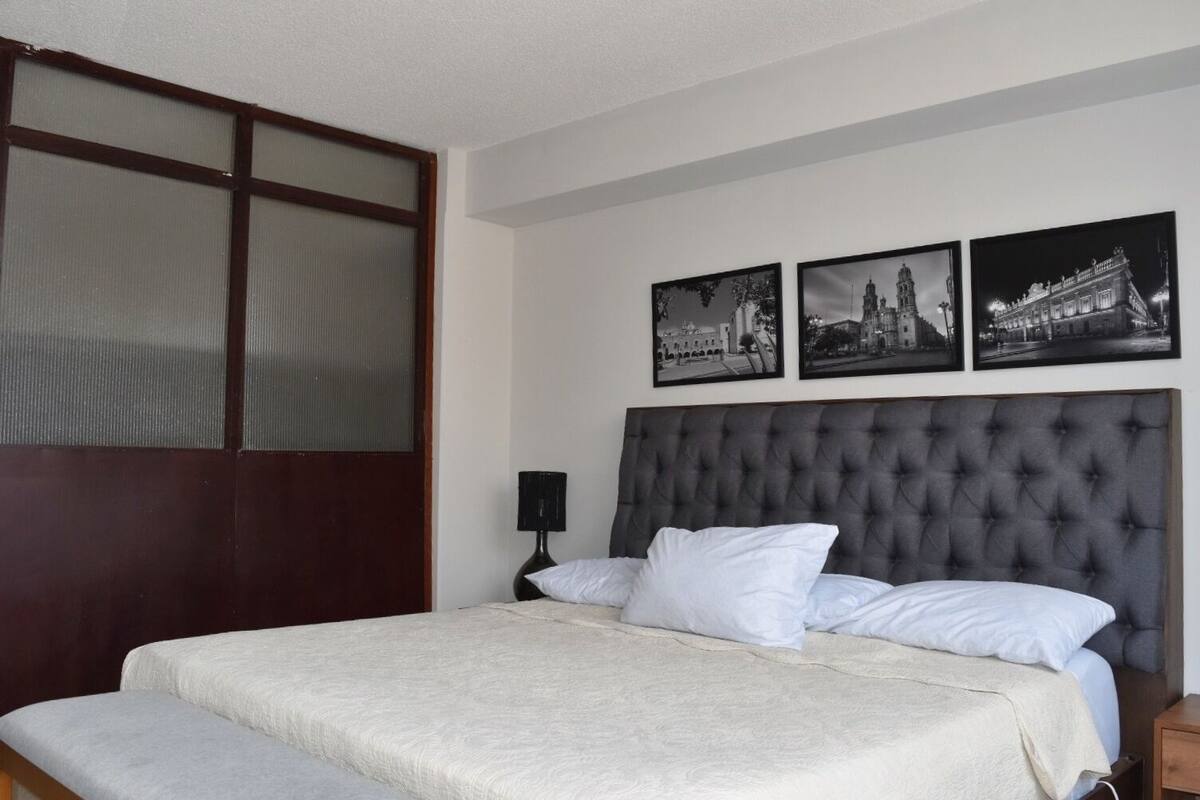 A hotel room with a large bed, a dark headboard, and three black-and-white photographs on the wall.