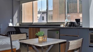 A compact room with a kitchenette, a dining area, and a large window offering a view of buildings.